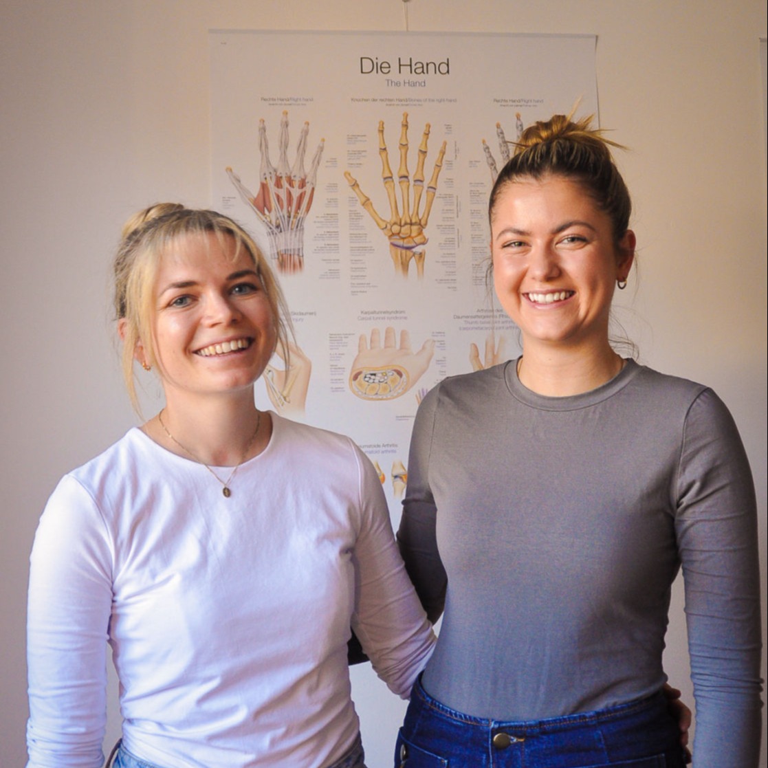 Lena Frank und Ihre Kollegin in der Praxis vor medizinischem Poster zur Handtherapie