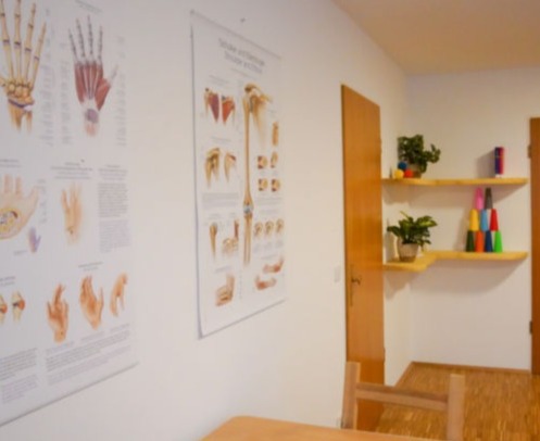 Therapieraum der Ergotherapie mit Anatomiepostern und Trainingsmaterial im Regal